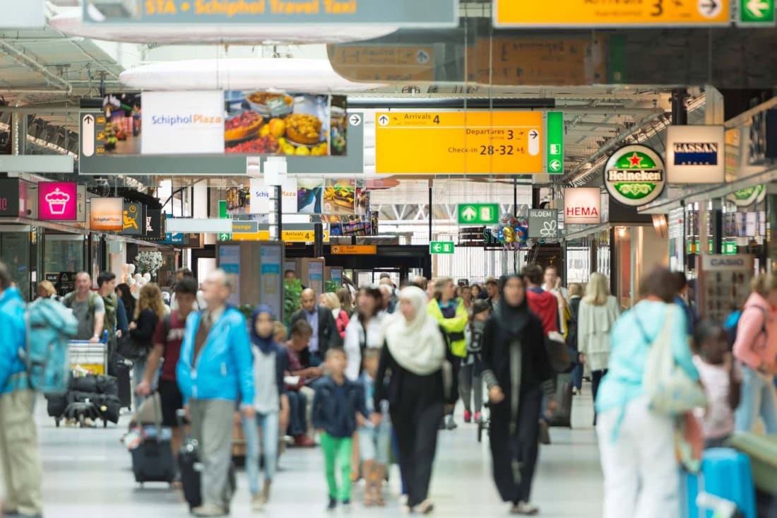 Busy airport hall with travellers and information boards.